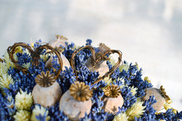 Closeup of beautiful dried valentine or wedding bouquet with poppy heads, lavender flowers and ivory phalaris grass decorated with two weaved rattan hearts, selective focus