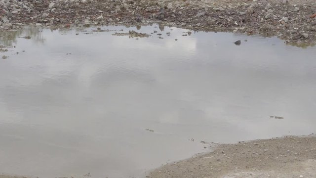 Dirty ground road with puddles and reflections.