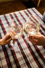 Friends clinking wine glasses above dinner table. Young couple drinking white wine in a cozy Italian restaurant.