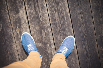 Look down view on blue shoes. Man standing on wooden bridge.