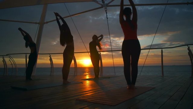 Silhouette group women practice tadasana asanas yoga class beach sea slow motion