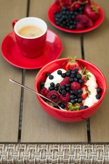 Healthy breakfast on garden furniture: cottage cheese with sour cream, strawberry, raspberry and blueberry, espresso and plate of fresh ripe berries on wooden garden furniture. Selective focus