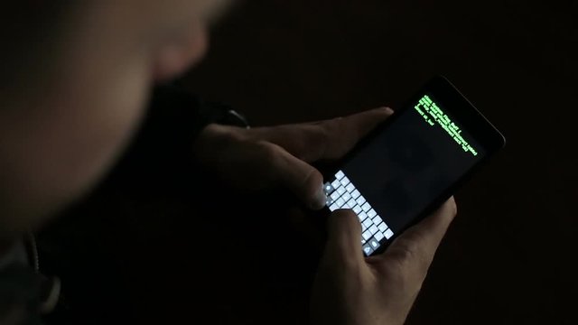 Hacker using a smartphone device to hijack. Green code hacking text overlapping
