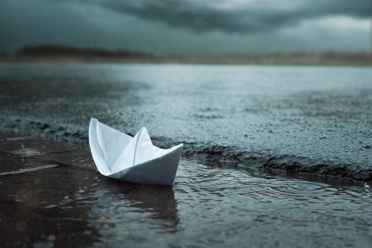 Papierschiff bei Regen in Stra&szlig;enrinne