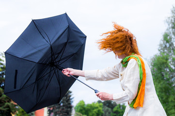 eine Frau mit roten Haaren versucht ihren Regenschirm festzuhalten - obrazy, fototapety, plakaty