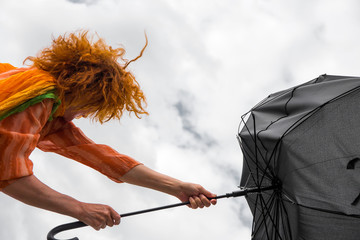 eine Frau mit roten Haaren hält bei Sturm ihren Regenschirm fest