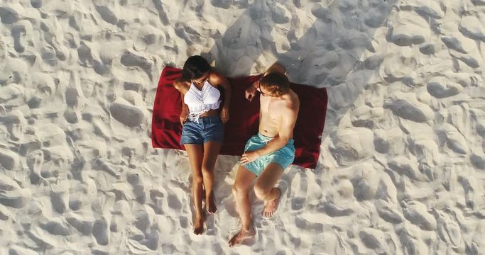 Top view of couple lying on white sand beach taking a sunbath in summer - drone shot