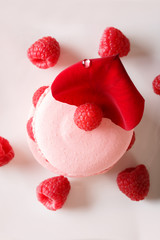 Delicious macaroon with fresh raspberries and rose petals close-up on a plate. vertical top view