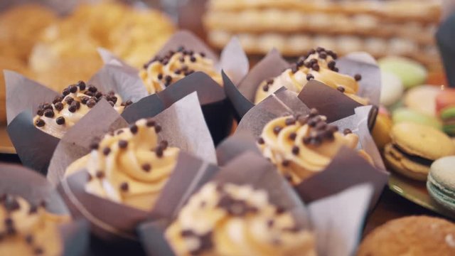 Chocolate puffs drops on buttercreme swirls on mini cakes wraped in purple paper in bakery on table, close up