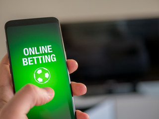 Online sports betting app on smart phone. Man holdning device.
