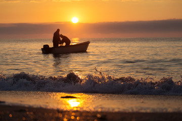 Naklejka na ściany i meble Two fishermen on a boat fishing on a sea with beautiful sunrise in background