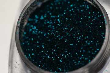 Closeup of teal nail makeup glitter in round jar isolated on silver background. Concept of beauty and makeup