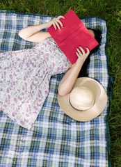 Woman reading a book and covering face outside on the grass