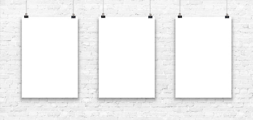 Three blank paper poster mockup on a white brick wall.
