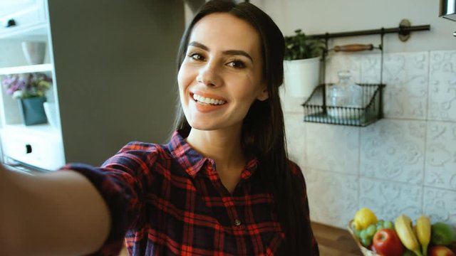 Attractive Smiling Woman Making Selfies, Photos On Her Device In The Kitchen At Home. Woman Blowing Kisses To The Camera. Close Up.