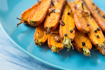 Roasted spring carrots on blue plate with garlic, pepper peas and coriander on wooden table. Selective focus
