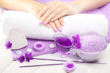 beautiful purple manicure with violet, candle and towel on the white wooden table.