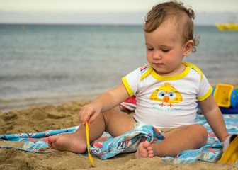 Little cute baby playing with sand near the sea at sunset