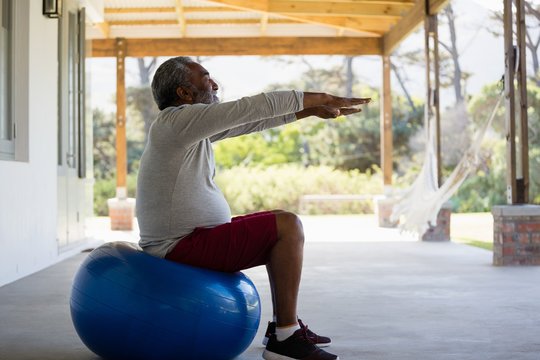 Senior man exercising on exercise ball in the porch - Powered by Adobe