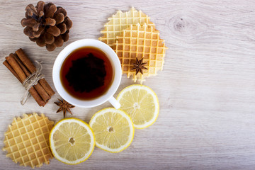 Obraz na płótnie Canvas Cup of tea with waffles and cinnamon, lemon, badian, pinecone