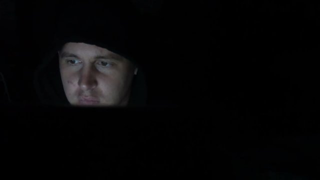 Male hacker working on a computer in a dark office room.