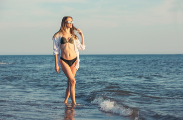 Attractive young woman walking along sea or ocean beach at sunset