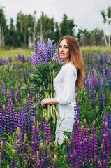 A girl in a white dress is standing among the lupines