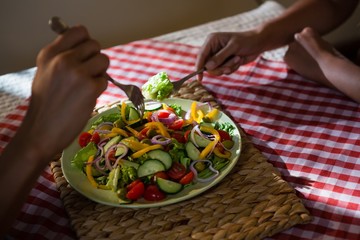 Cropped hands of friends having salad at table