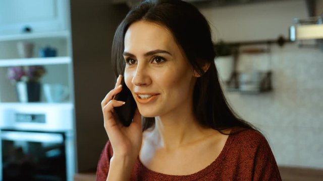 Beautiful caucasian woman talking on the phone while cooking denner in the kitchen. Close up