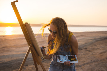 Obraz premium Young woman artist painting landscape in the open air on the beach