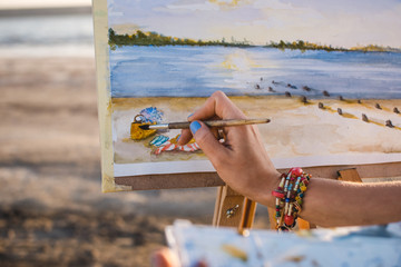 Obraz premium Young woman artist painting landscape in the open air on the beach, close up