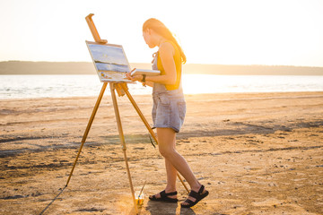 Obraz premium Young woman artist painting landscape in the open air on the beach