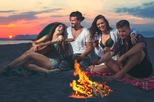 Friends Around The Fire In Sunset On Beach