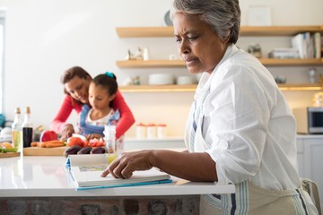 Senior woman looking at recipe book in kitchen