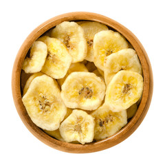 Dried banana chips in wooden bowl. Yellow deep fried slices of bananas, covered with sugar or honey. Snack with sweet taste. Isolated macro food photo close up from above on white background.