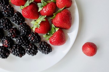 Delicious, fresh strawberries  and blackberries with green leaves on the white table