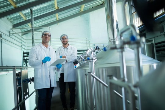 Portrait of scientists with clipboard standing by storage tank