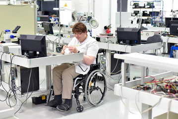 Rollstuhlfahrer am Arbeitsplatz in einer Fabrik zur Montage von Elektronik - Alltag mit...
