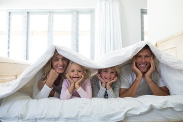 Obraz na płótnie Canvas Portrait of happy family lying under blanket on bed in bedroom