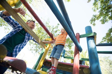 Father looking at son walking on jungle gym at playground