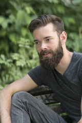 Handsome thoughtful bearded guy sitting on a bench in park