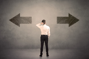 Business man taking a decision while standing in front of two grungy arrows on wall