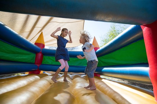 Happy siblings jumping on bouncy castle at playground