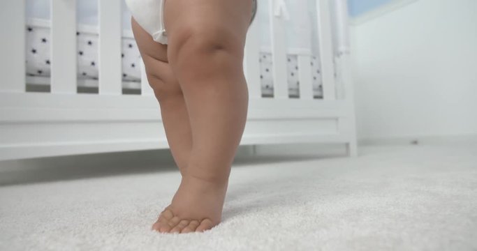 Baby Legs Learning to Walk Off Screen. a close up of lower half of baby assisted learning balance and walking off screen
