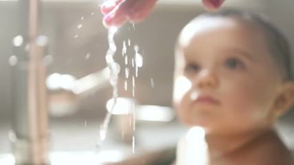 Mother Hand Checks Water Temp with Child. a close up of a woman's hand testing and feeling the temperature of the water while a child looks on in the background. Slow motion
