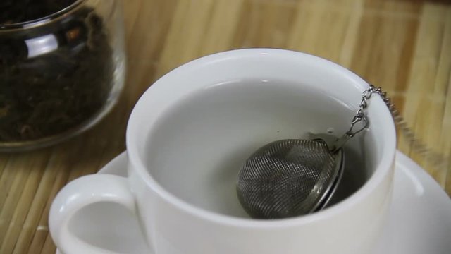 Strainer being dropped in and out of white cup.