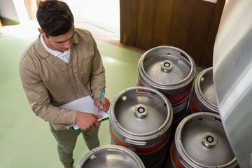 High angle view of worker writing on clipboard by kegs