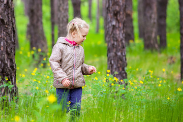 Cute little blonde girl walking in a wild forest between trees and flowers