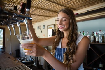 Happy barmaid pouring beer from tap in glass