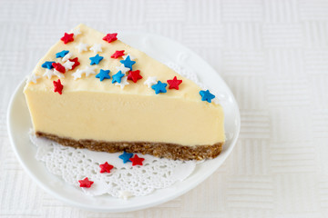 Obraz na płótnie Canvas Slice of plain new york cheesecake on white plate served for celebration of Veteran's Day or July 4th in USA. Selective focus